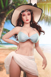 Asian supermodel love companion Chiaki, standing on the beach in a white wrap and light blue bikini top and wide-brimmed hat.