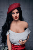 Lovely white skin and black haired sex doll Bluma, in a wine colored painter hat and boat neck grey top, cupping her large left breast with her left hand.