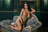 High fashion model and icon Dominika, kneeling on the sitting room divan with the top of her gold swimsuit pulled down to reveal big luscious boobs.
