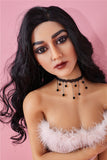 5ft tall Dasia, a white skinned sex doll with an athletic build, looking directly at the viewer in a furry low cut top, black choker necklace and black, wavy hair.