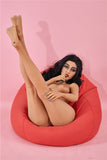 Dasia naked, lying back on a red bean bag cushion with her legs raised straight up and crossed.