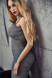 5ft 7in blonde sex doll Sophiea, in a gray dress, medium shot with her back to a wall.