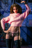 5ft 6in red-haired goddess sex doll Kiera, in a half-cut pink knit sweater and leopard print underwear and black leggings with one hand on her hip and the other over her head.