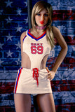 168cm 5ft 6in Katja, a white skin sex doll with an athletic figure and blonde hair standing in front of a brick wall painted over in the American flag. Katja wears a kinky, white cheerleader outfit.