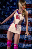 Katja, wearing a white mini-dress with cutout sides and pink knee pads, dancing in front of a stripper pole before a brick wall painted over with the US flag.